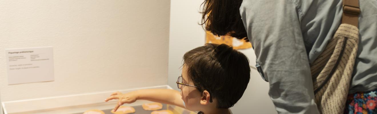 Lors du vernissage de l'exposition un enfant devant une vitrine avec ses parents pointe du doigt l'œuvre qu'il a réalisée